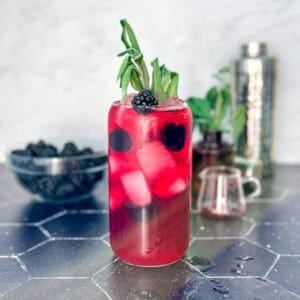 A blackberry sage refresher on a black counter with a accoutrements behind.