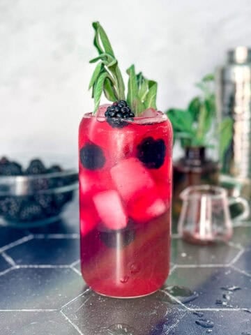 A blackberry sage refresher on a black counter with a accoutrements behind.