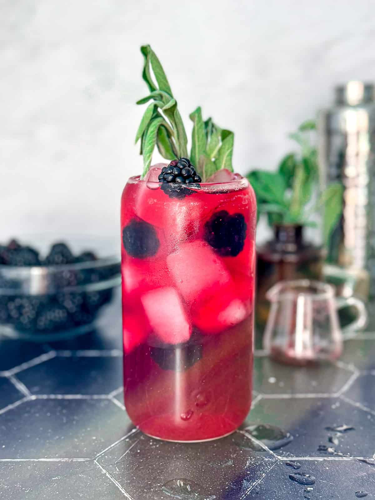 A blackberry sage refresher on a black counter with a accoutrements behind.