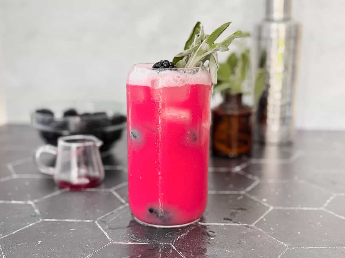 A midnight version of the blackberry sage refresher on a black counter with a accoutrements behind.