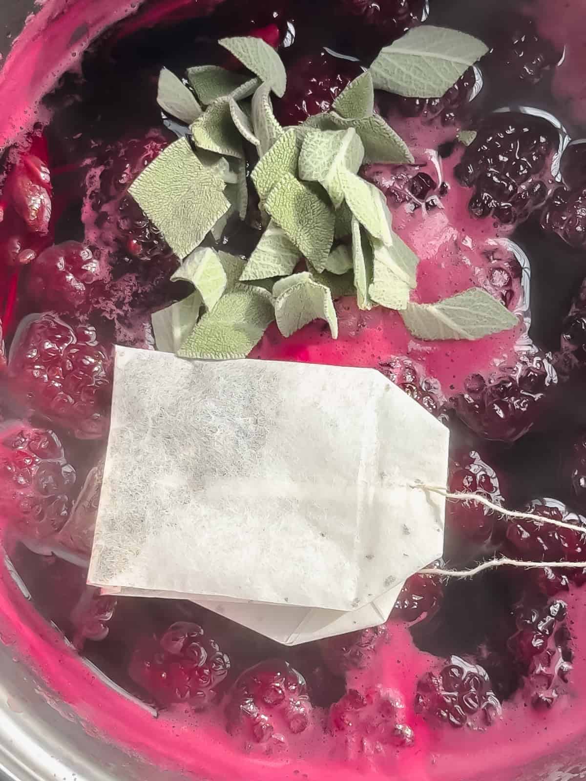 Adding green tea bags and chop sage to blackberry sage simple syrup.