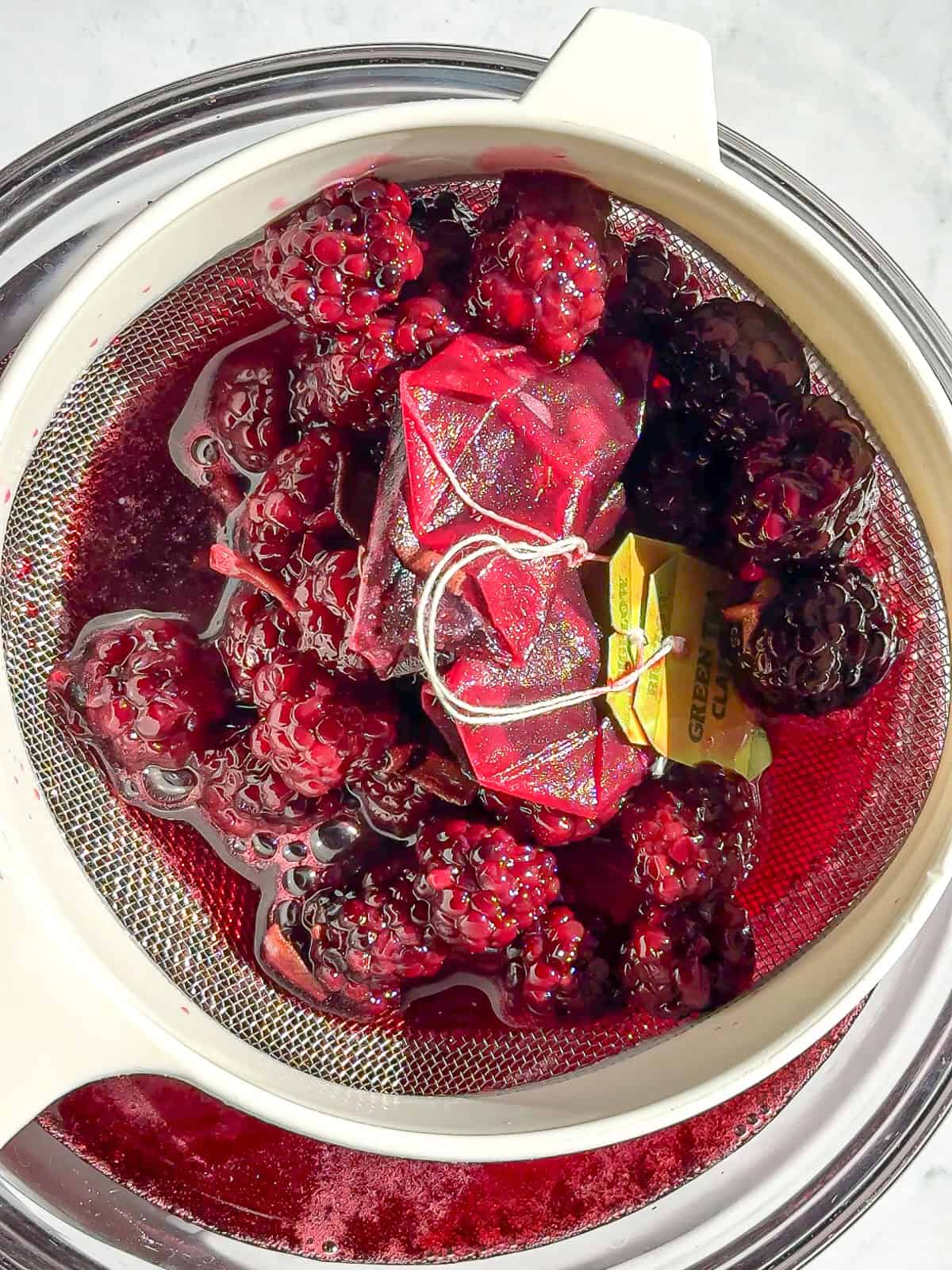 Straining the berries, tea bags, and sage leaves from the blackberry sage simple syrup.