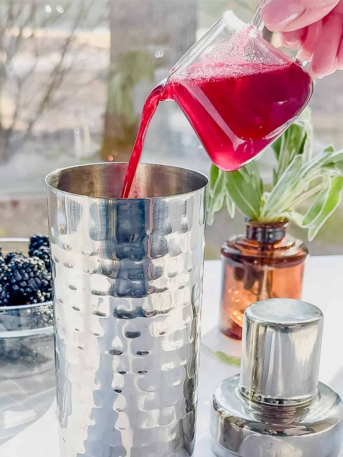 Pouring blackberry sage syrup into a cocktail shaker.