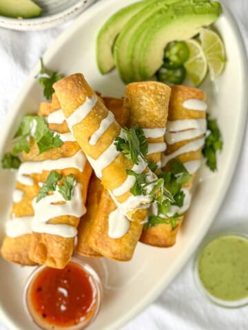 Breakfast taquitos on a platter with avocado and two salsas.