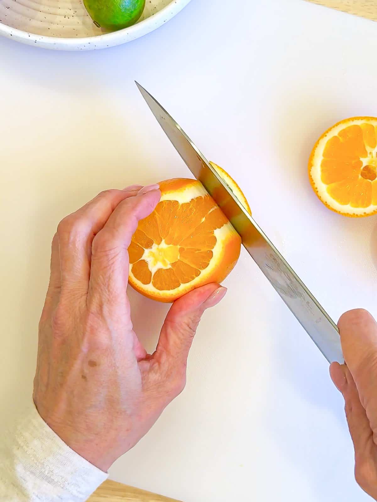 Using a sharp knife to slice off the peel and white portion of an orange.