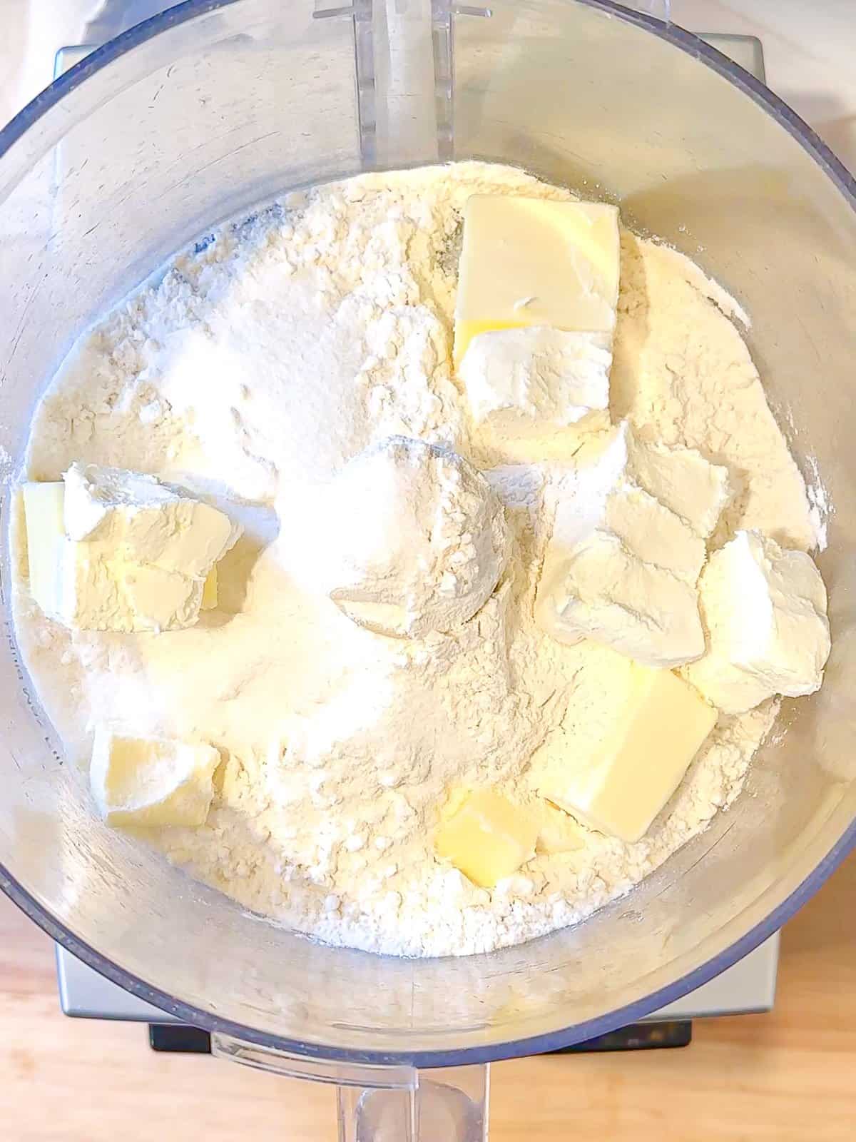 Adding cream cheese and butter to dry ingredients to make a cream cheese crust in a food processor.