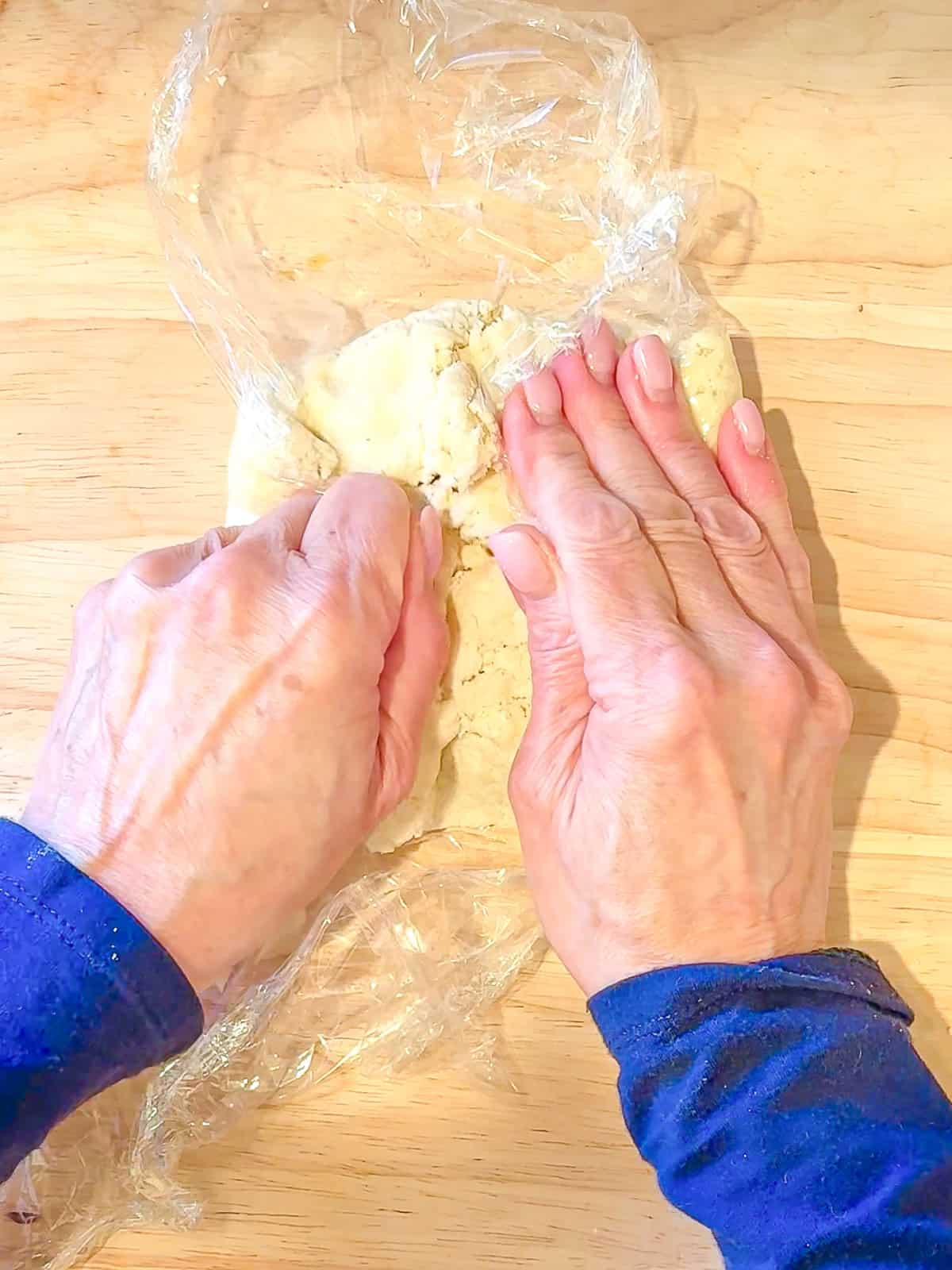 Using plastic wrap and my hands to form a cream cheese crust dough disc.