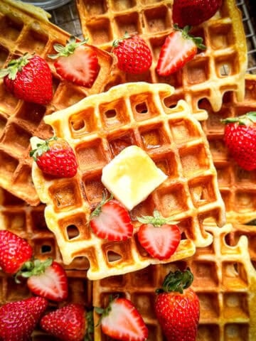 Top view of a sheep pan covered with classic waffles with strawberries, butter, and maple syrup.