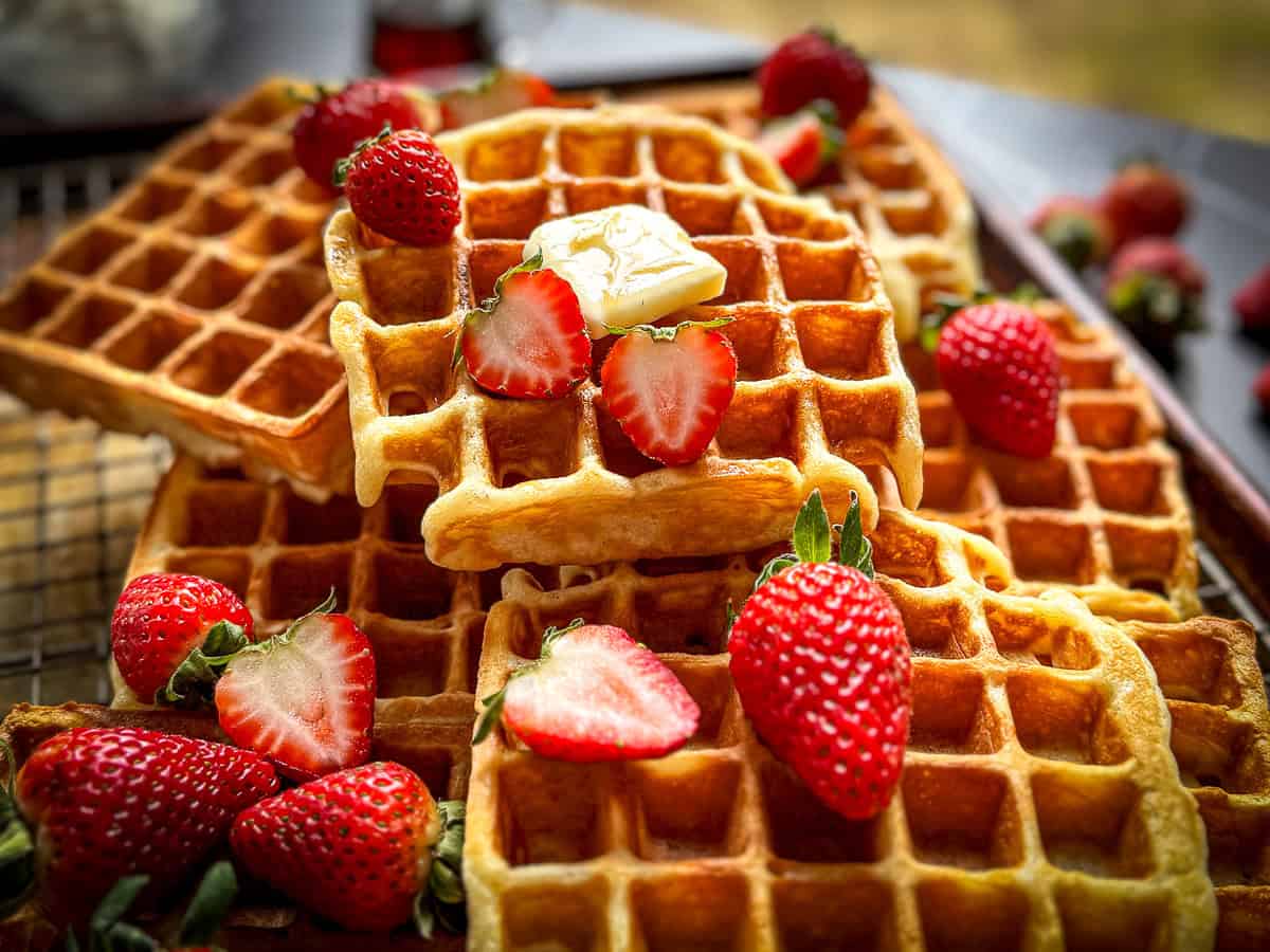 45° angle view of a sheet tray filled with waffles topped with strawberries and butter and maple syrup.