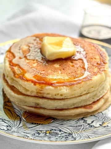 Side view of applesauce pancakes with a pat of butter and maple syrup.