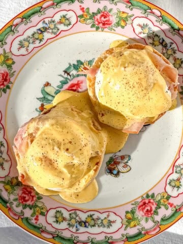 Eggs Benedict with hollandaise sauce on a floral plate.