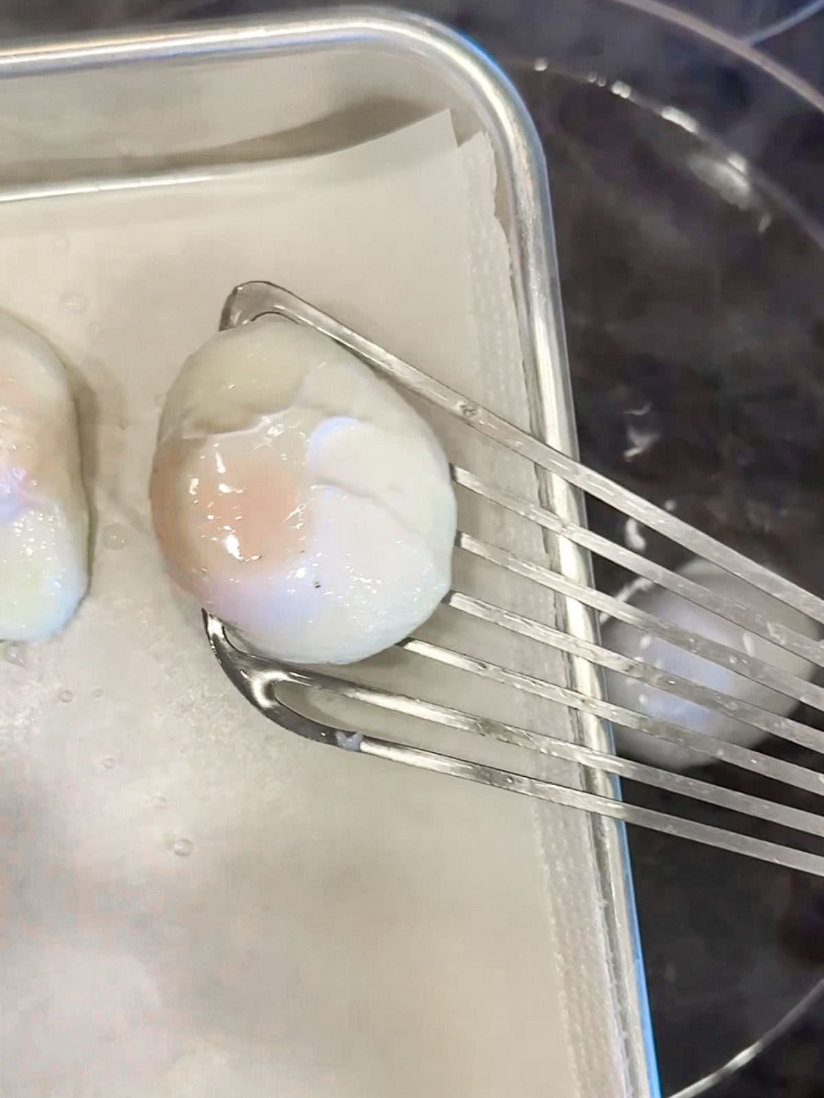 Using a slotted spatula to place a poached egg on paper towel to dry.