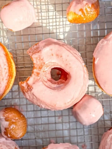 An orange glazed donut with a bite taken out of it on a wire rack.