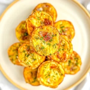 A stack of mini quiche Lorraine on a white plate with a tan rim.