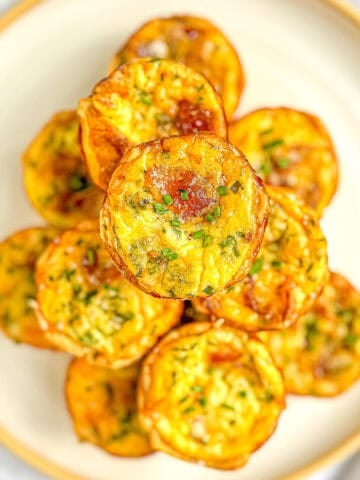 A stack of mini quiche Lorraine on a white plate with a tan rim.