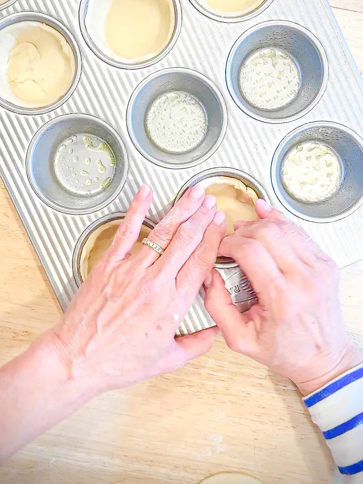 Pressing circles of pie dough into a lightly greased muffin pan.