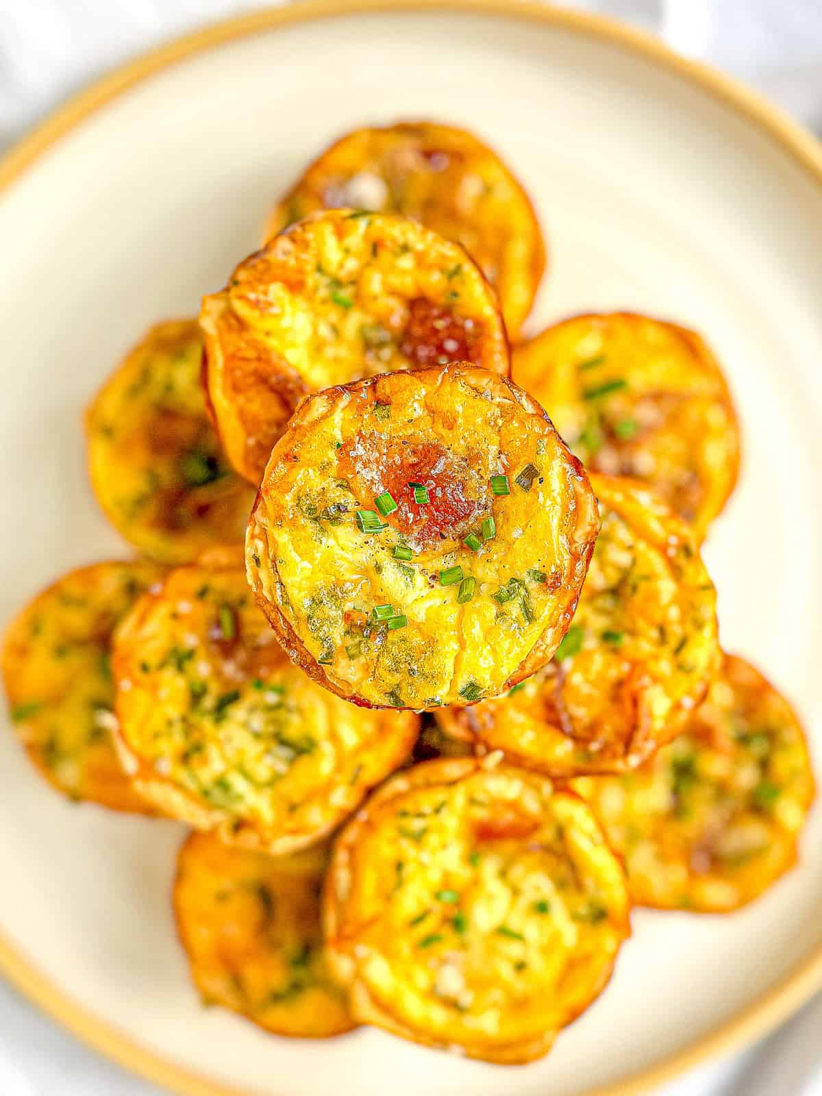 A stack of mini quiche Lorraine on a white plate with a tan rim.