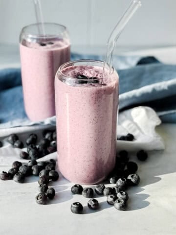 Two blueberry smoothies on a white background with blueberry scattered about.