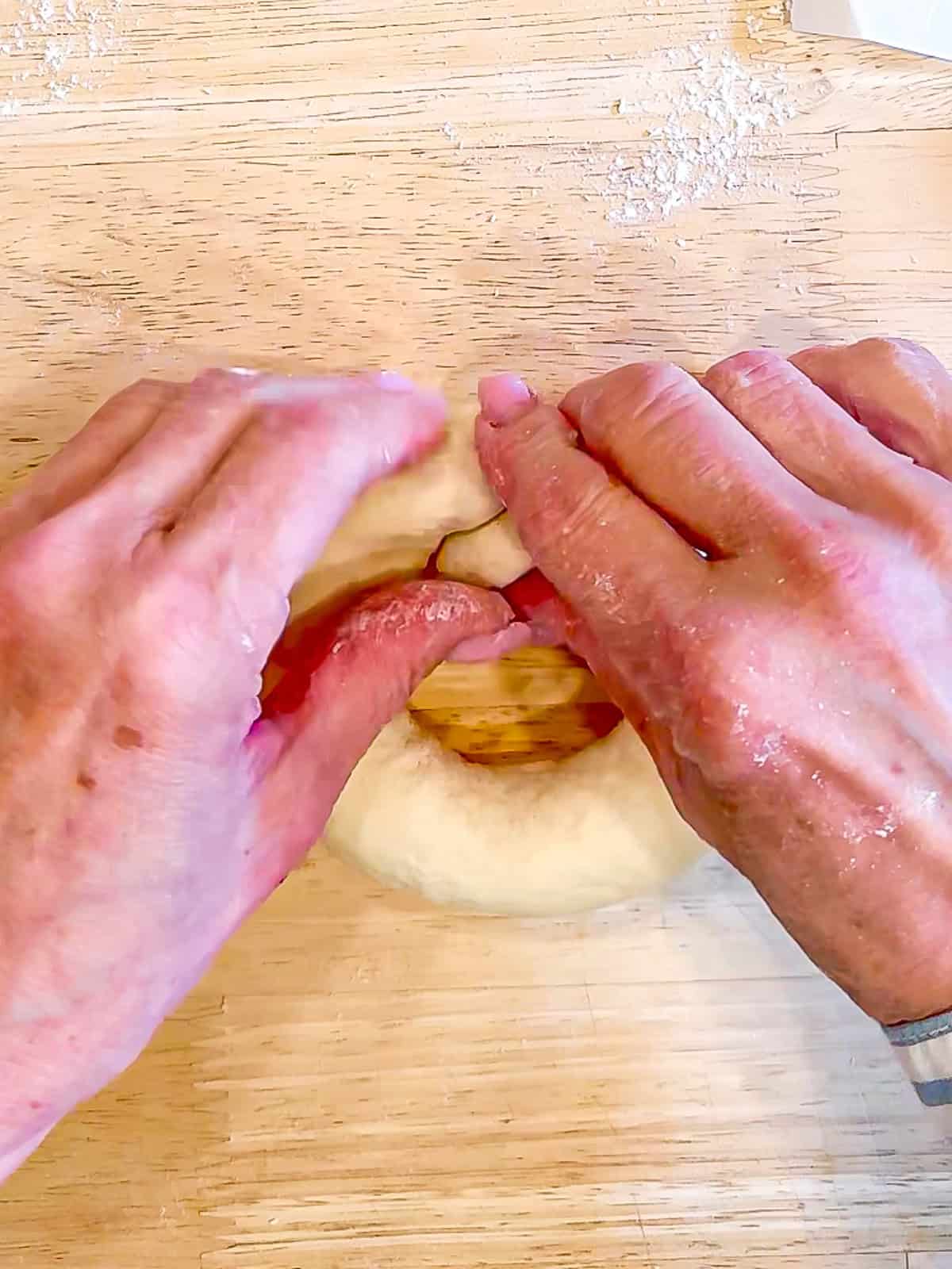 Joining the ends of a long rope of dough to make a bagel shape.