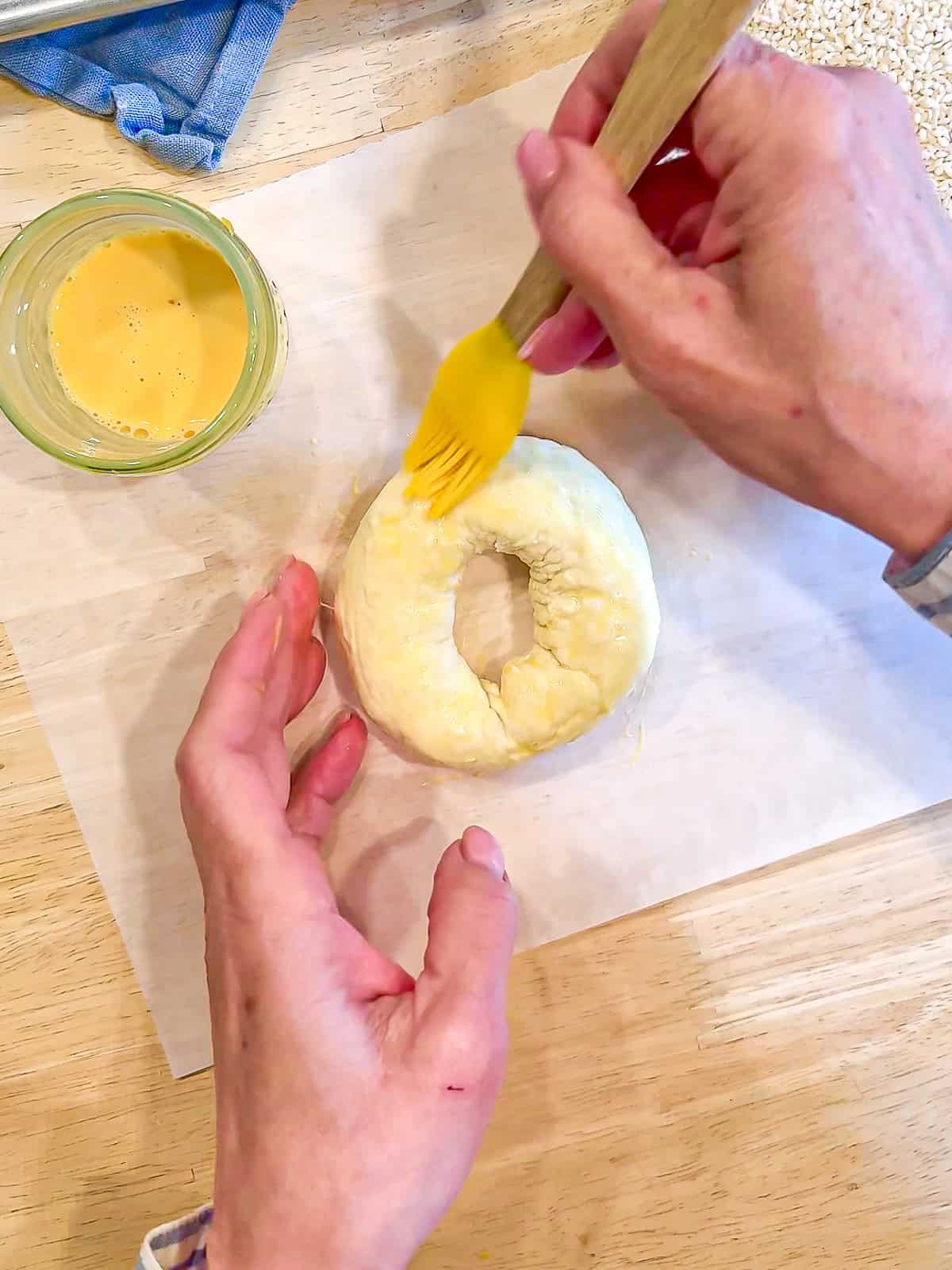 Placing an egg wash on a cottage cheese bagel with a yellow pastry brush.