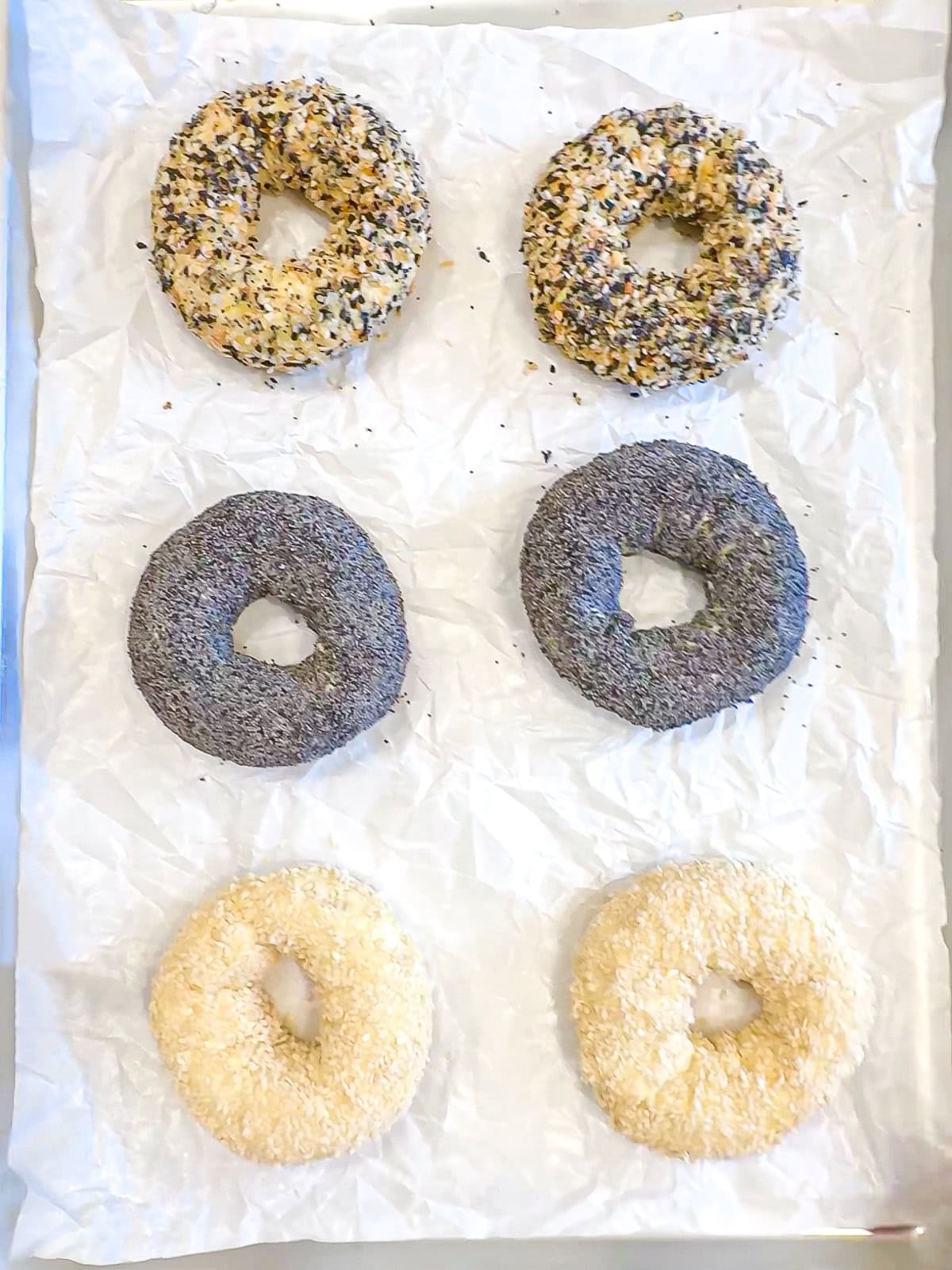 Cottage cheese bagels with toppings on a parchment paper lined sheet pan ready to go into the oven.