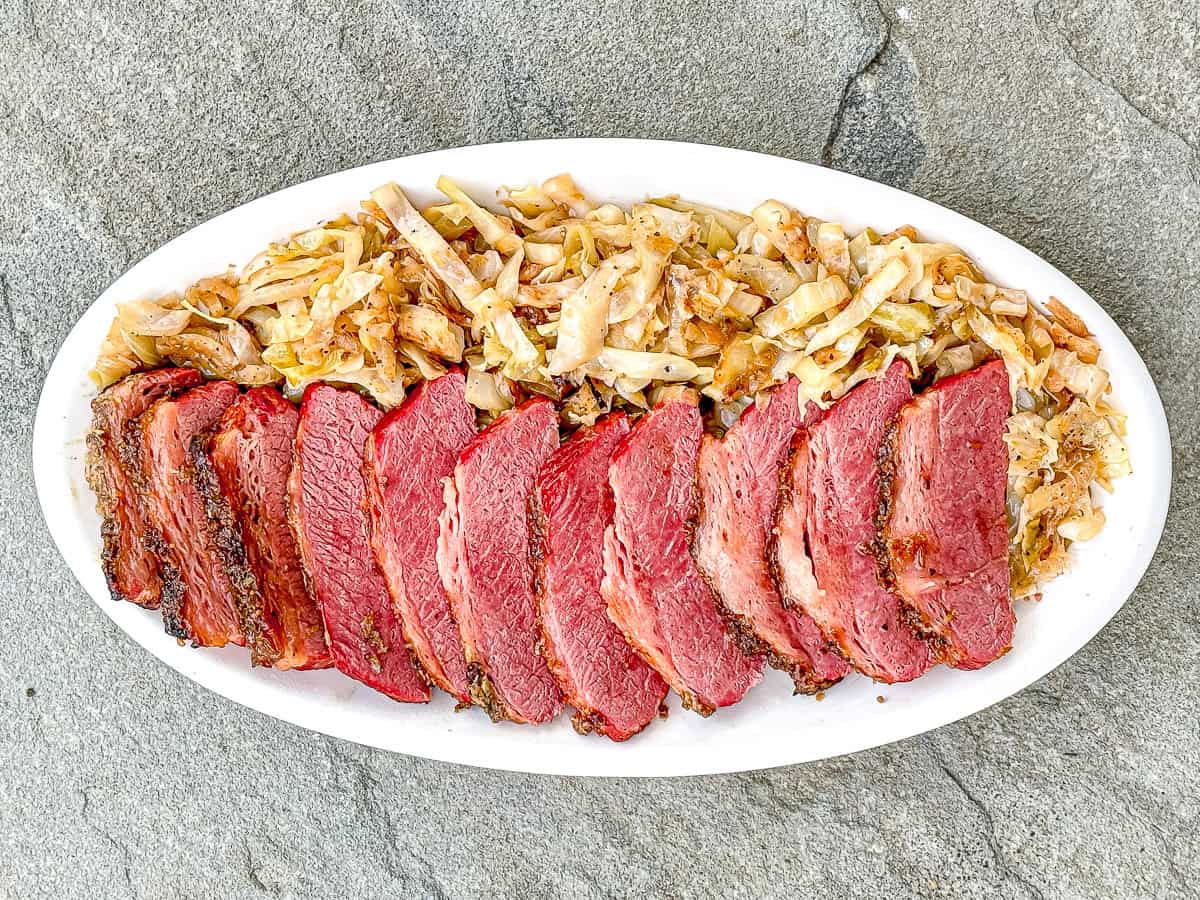 A platter containing slices of crispy corned beef and sautéed southern fried cabbage.