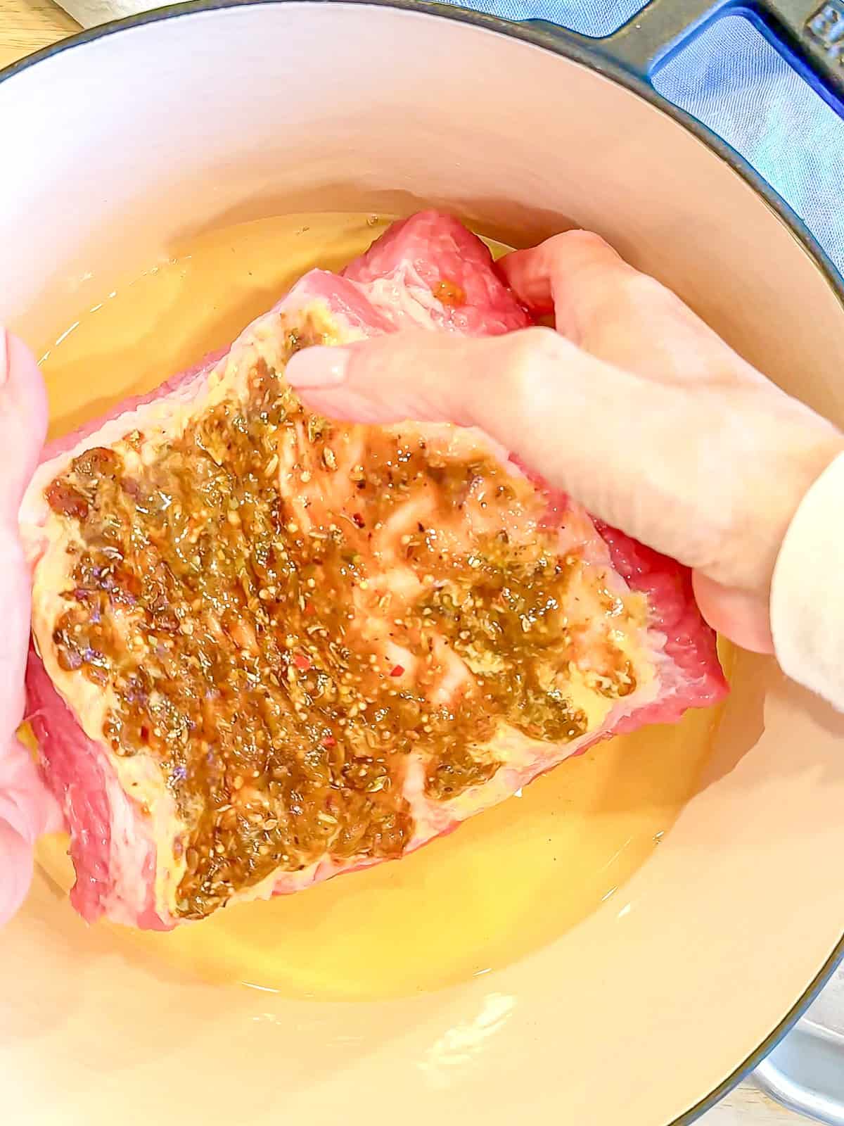 Placing the seasoned corned beef brisket into a Dutch oven containing apple juice and apple cider vinegar.