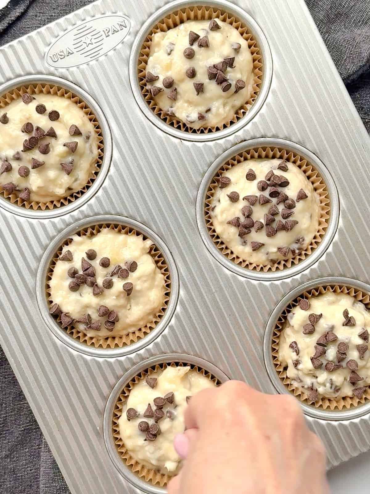 Sprinkling chocolate chips on top of muffin batter in a muffin pan.