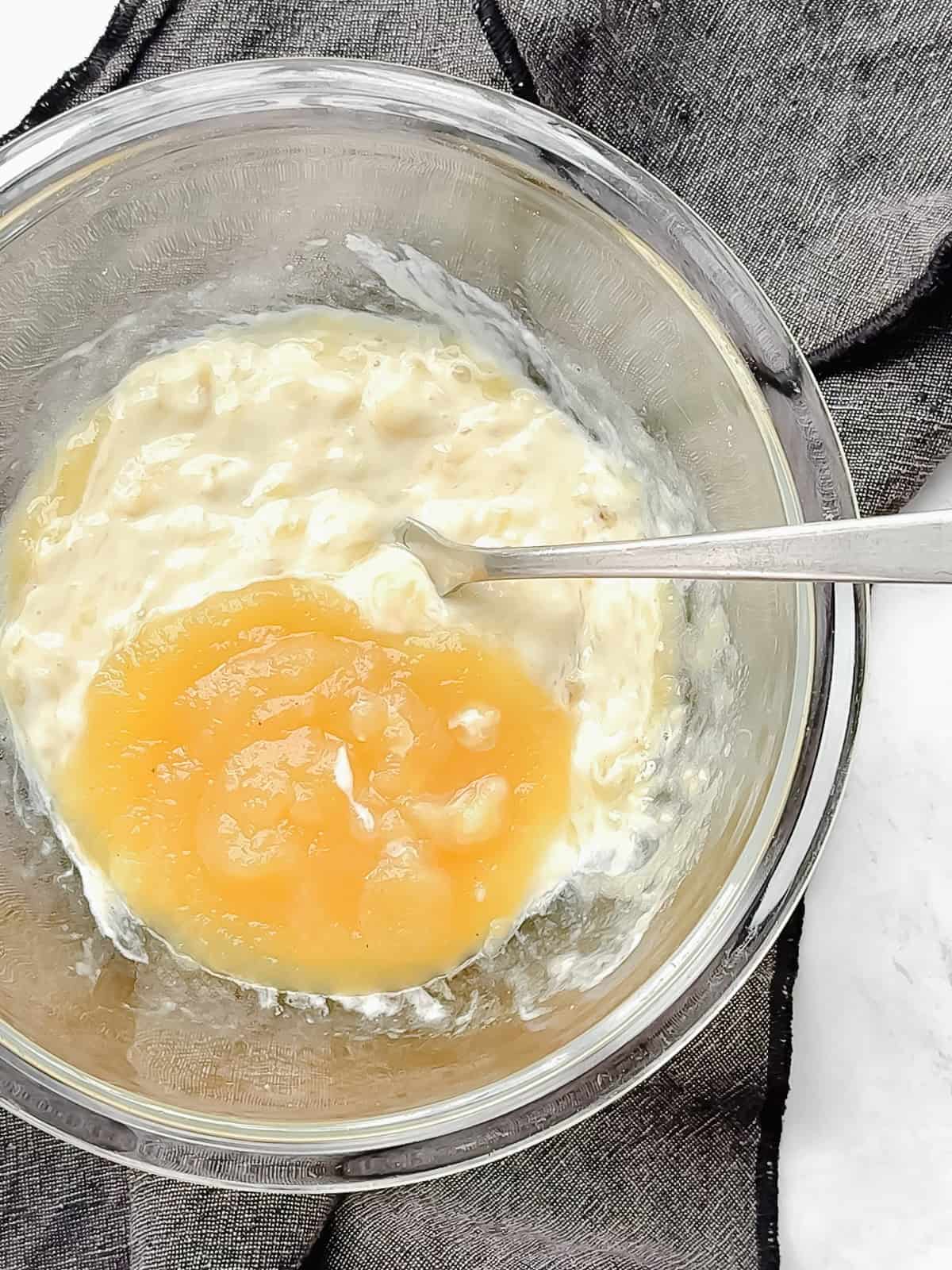Adding applesauce to mashed bananas and yogurt to make four ingredient banana muffins without egg.