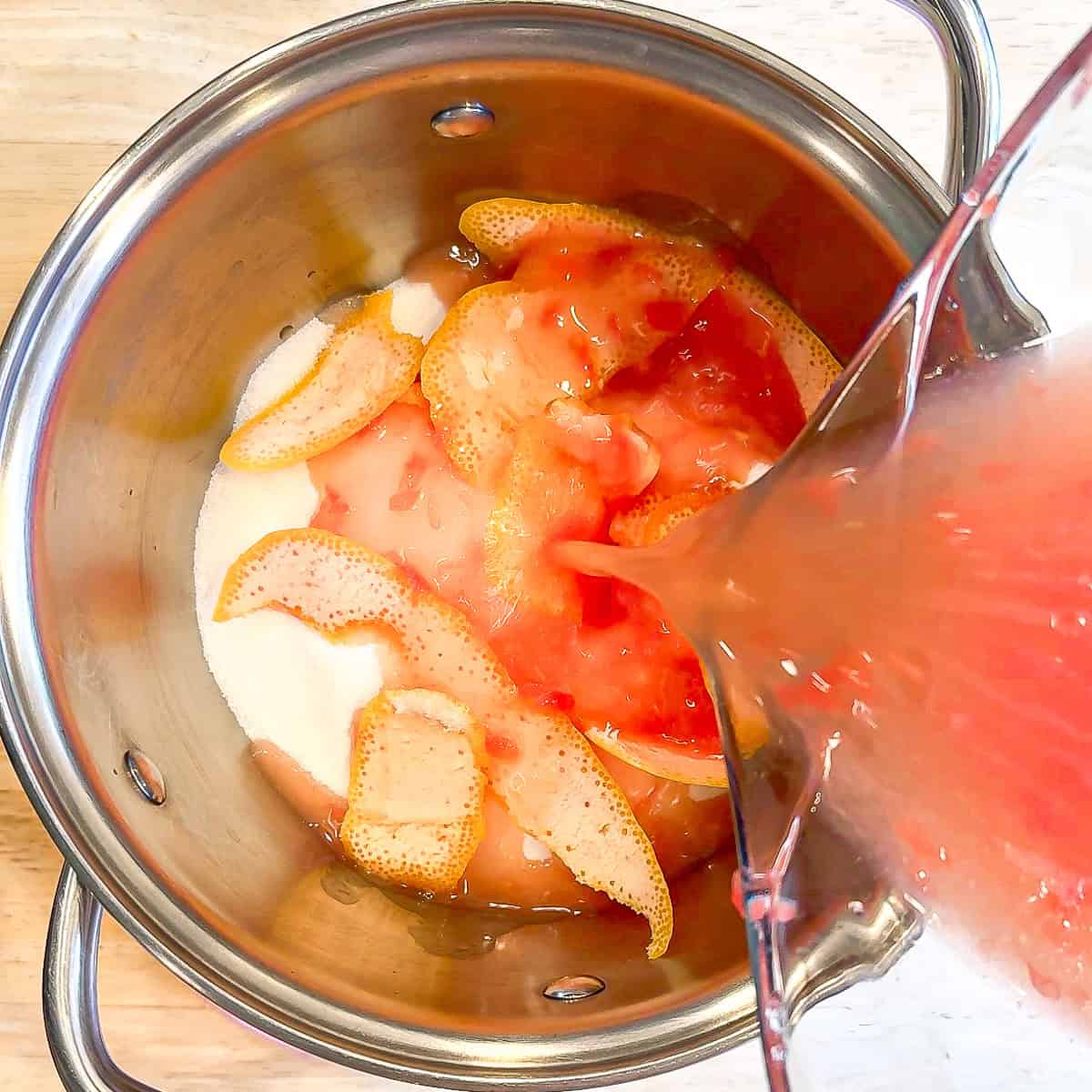 Adding sugar, grapefruit peels, and grapefruit juice to a small saucepan to make grapefruit simple syrup.