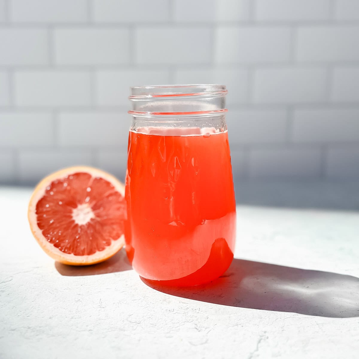A mason jar of grapefruit simple syrup with a half of a grapefruit on the counter next to it.