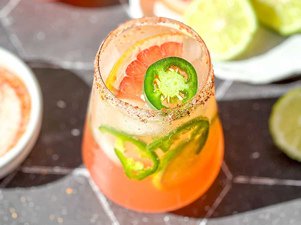 Spicy Paloma mocktail with a grapefruit and jalapeño garnish sitting on a black surface.