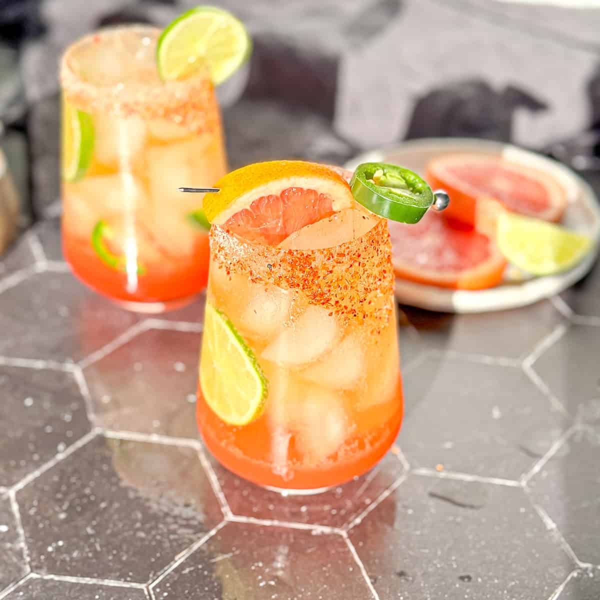 Spicy Paloma mocktails with a grapefruit and jalapeño garnish sitting on a black surface.