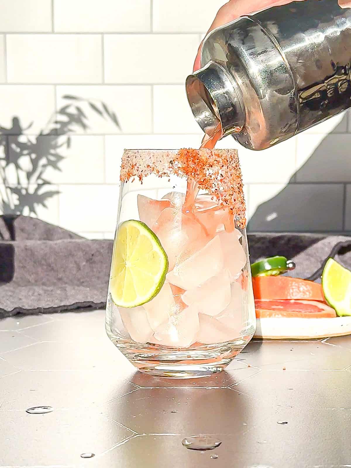 Pouring shaken ingredients for a spicy Paloma Mocktail into a glass with ice and a lime slice.