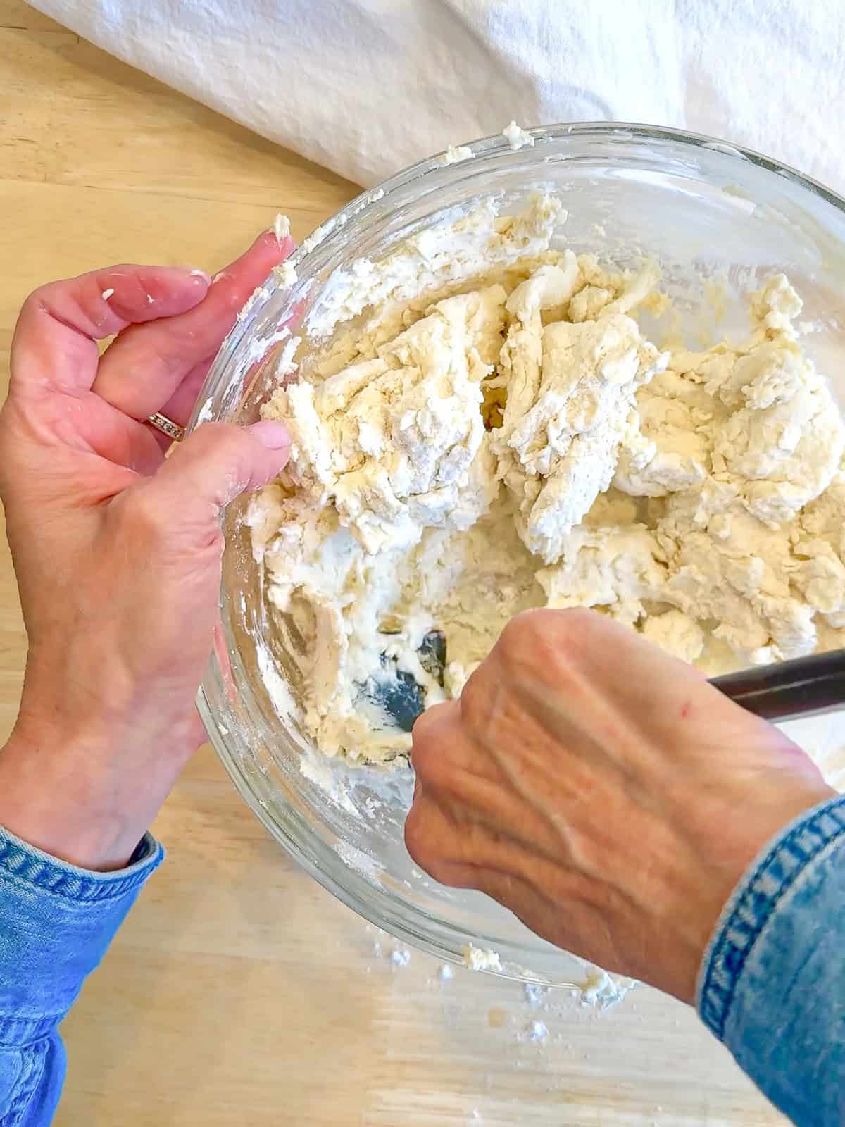 Using a silicone spatula to mix together two ingredient dough in a glass bowl.