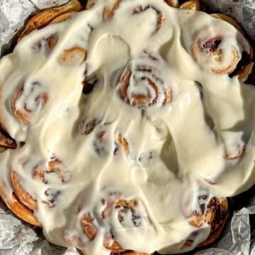 Quick cinnamon rolls with cream cheese frosting in a parchment paper lined cast-iron pan.