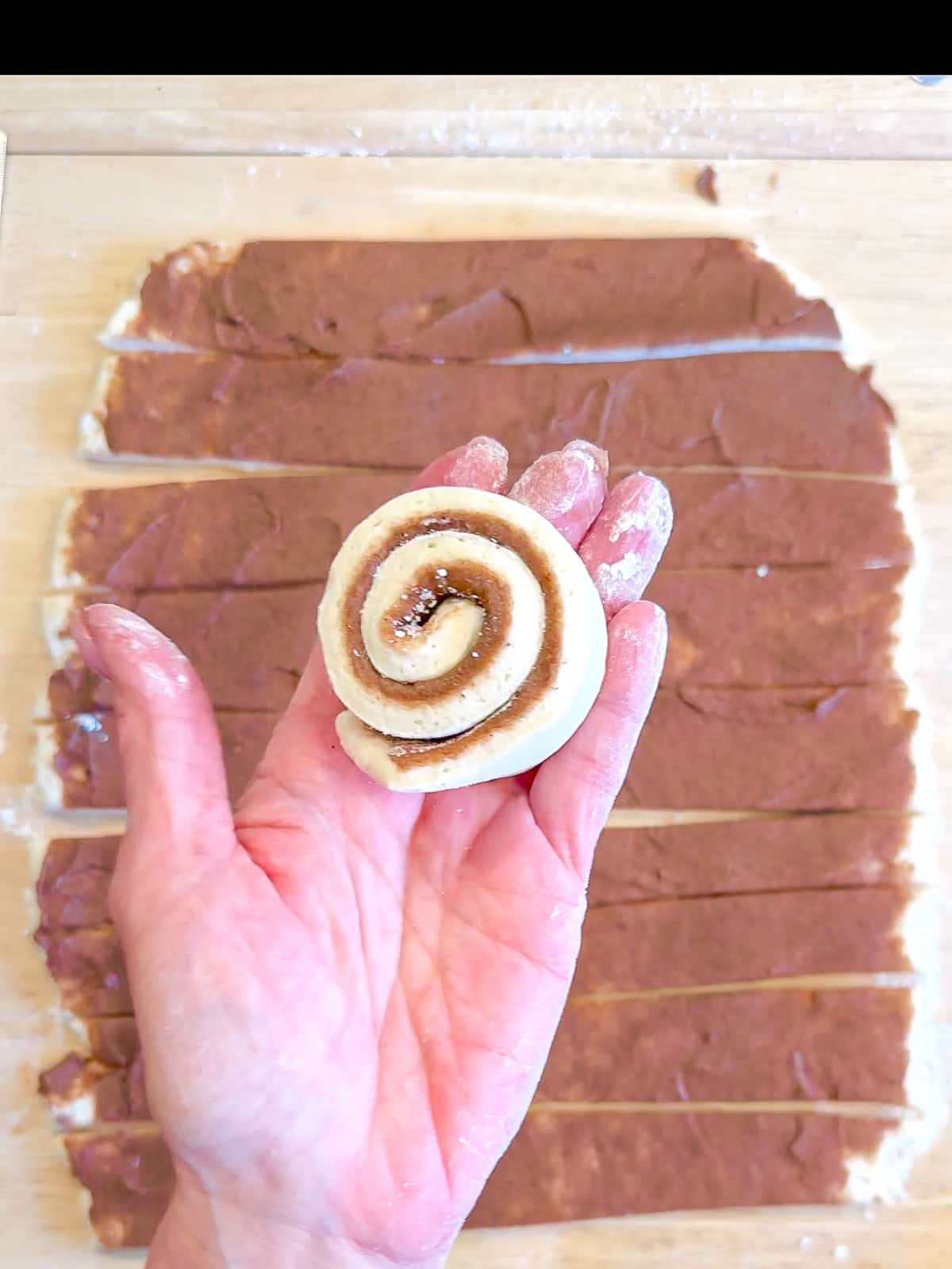 Author's hand holding a spiral of cinnamon roll dough.