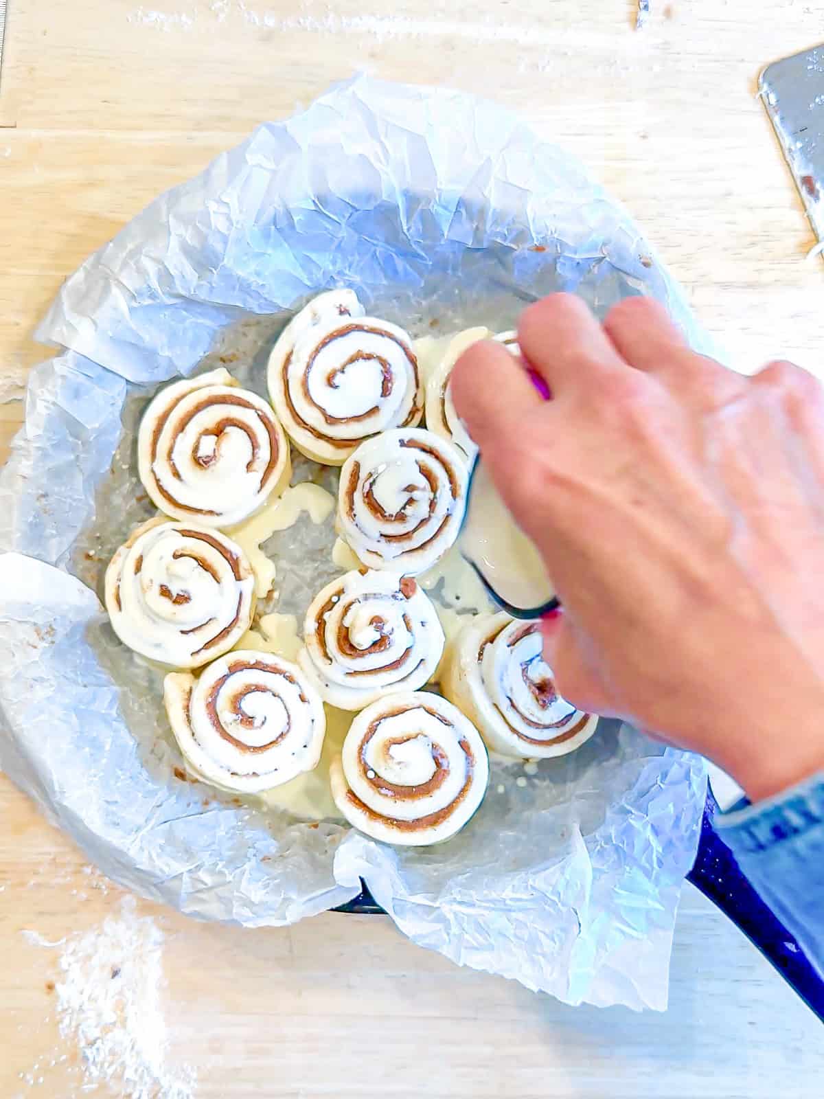 Pouring heavy cream over cinnamon rolls in a cast-iron pan before baking.