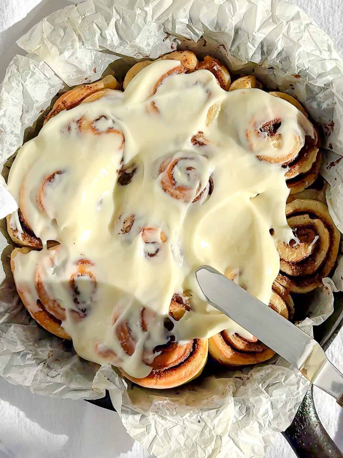 Spreading cream cheese frosting on top of quick cinnamon rolls.