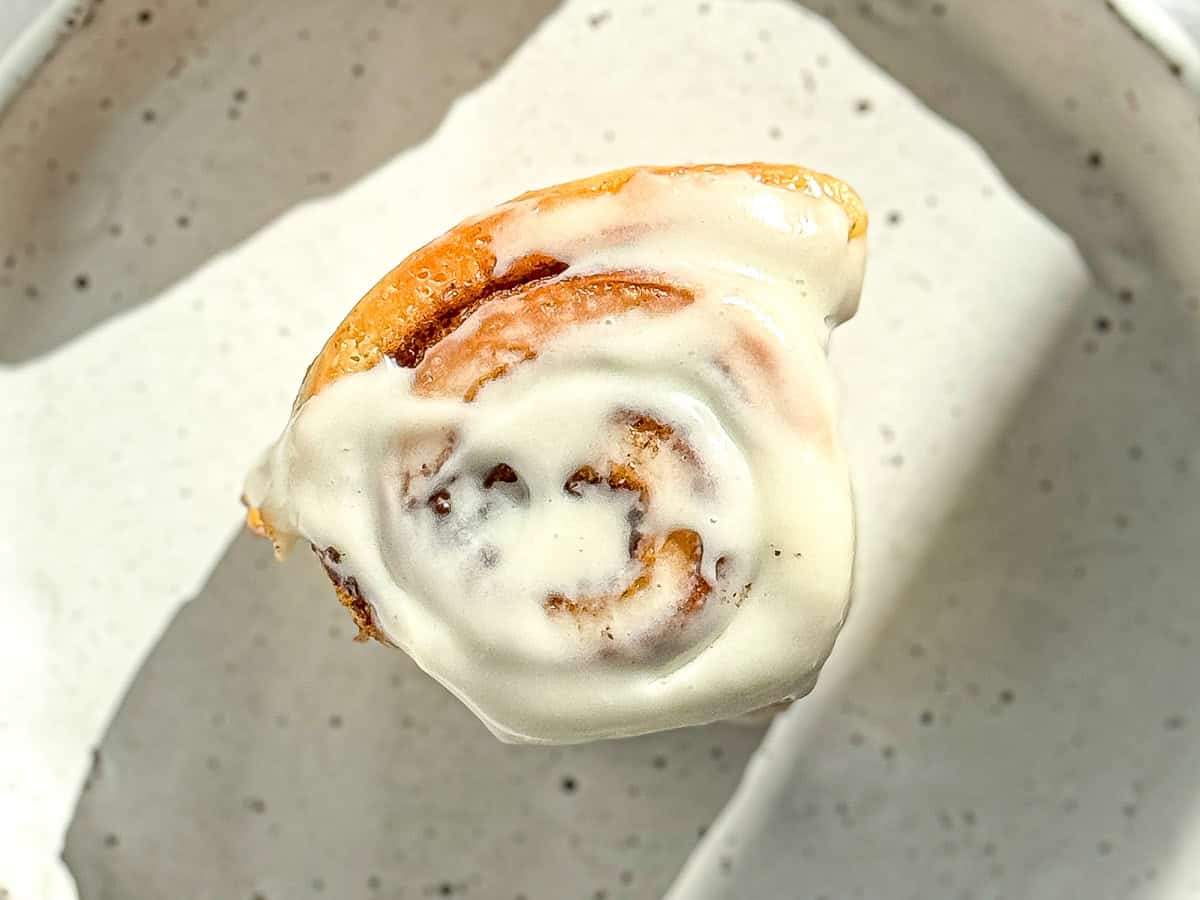 Quick cinnamon roll with cream cheese frosting sitting on a white speckled plate.