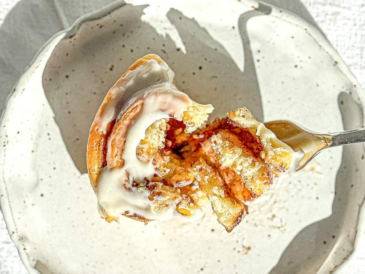 A cut open quick cinnamon roll with cream cheese frosting sitting on a white plate.