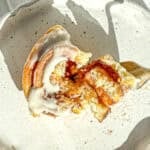 A cut open quick cinnamon roll with cream cheese frosting sitting on a white plate.