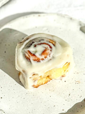 A quick cinnamon roll with cream cheese frosting sitting on a white plate.