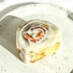 A quick cinnamon roll with cream cheese frosting sitting on a white plate.