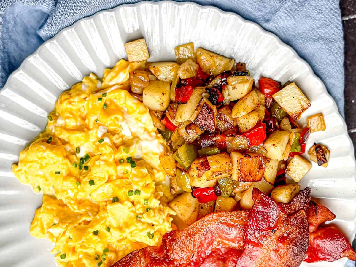 Potatoes O'Brien on a plate with creamy cottage cheese eggs and crispy bacon.