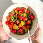 Author's hands holding a white bowl containing balsamic tomato salad and a spoon.