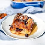 A slice of blueberry croissant baked French toast drizzled with maple syrup on a white plate.