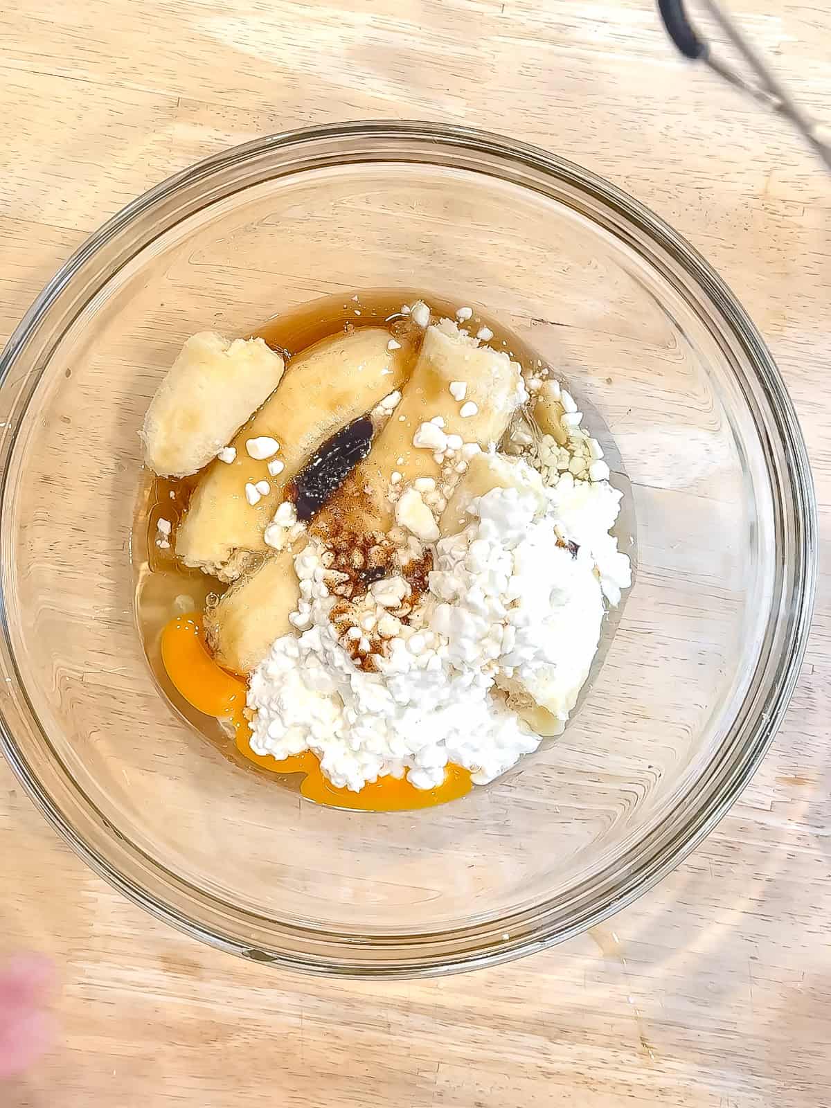Bananas, eggs, cottage cheese, vanilla, and maple syrup in a glass bowl to make banana breakfast cake.