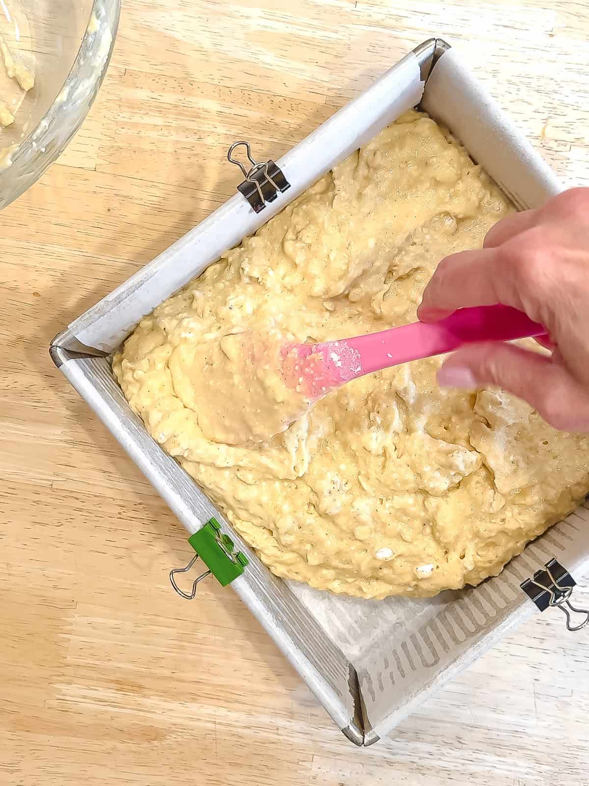 Spreading banana breakfast cake batter into the bottom of a parchment lined baking pan.