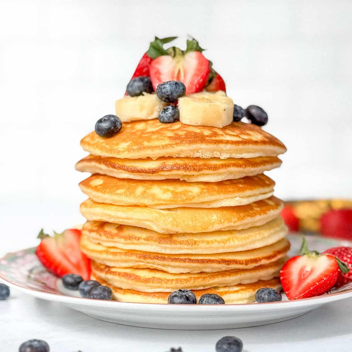 A stack of condensed milk pancakes with fruit on top and around the base.